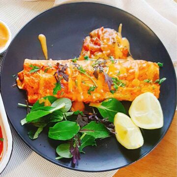 mushroom enchiladas served in a black plate topped with fresh greens