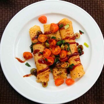 vegan savory crepes served in a white plate topped with cherry tomatoes, olives and cilantro leaves.