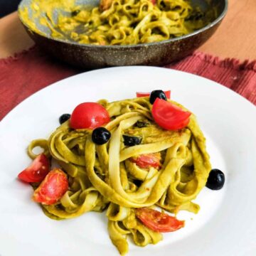 vegan spinach pasta served in white plate topped with cherry tomatoes and black olives