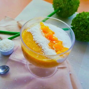 Semolina pudding served in a glass jar topped with coconut cream, mango slices and coconut shreds.