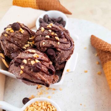 Chocolate nice cream scoops served in a white bowl with cones on side