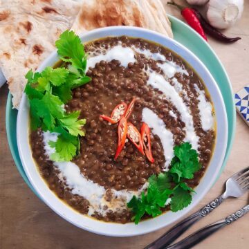 Brown Lentil curry served in a bowl topped with coconut cream, cilantro leaves and chili.