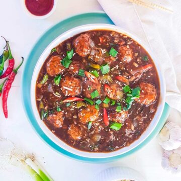 Veg Manchurian served in a white bowl with chilies and spring onion on top