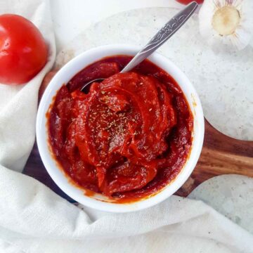 Vegan pizza sauce served in a white bowl placed on a wooden board.