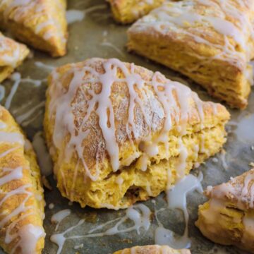 eggless pumpkin scones on a baking tray with maple glaze drizzled on top.