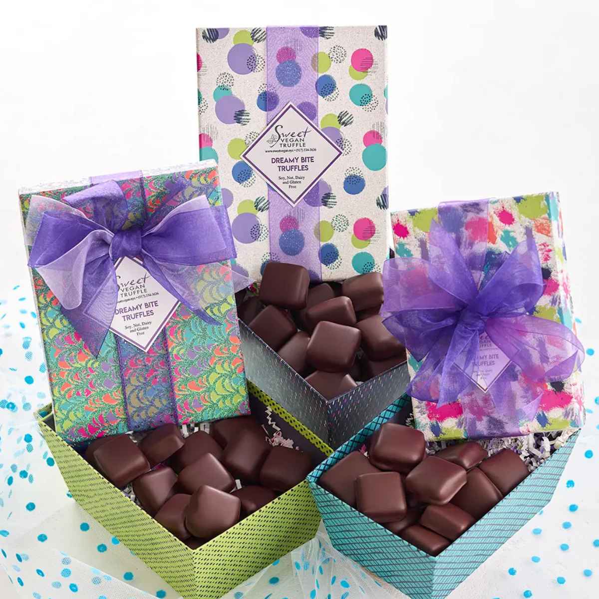 A colorful assortment of gift boxes filled with chocolate truffles, tied with purple ribbons, set against a light backdrop.
