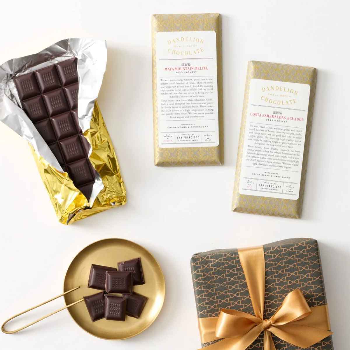 An arrangement of Dandelion Chocolate bars, a golden-wrapped bar, a plate with chocolate squares, and a beautifully wrapped gift.