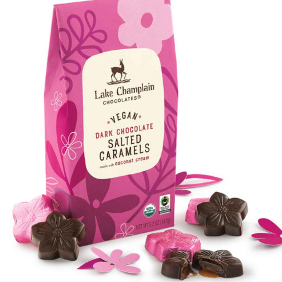 A pink bag of Lake Champlain vegan dark chocolate salted caramels, with chocolate and pink flower-shaped candies scattered around it.