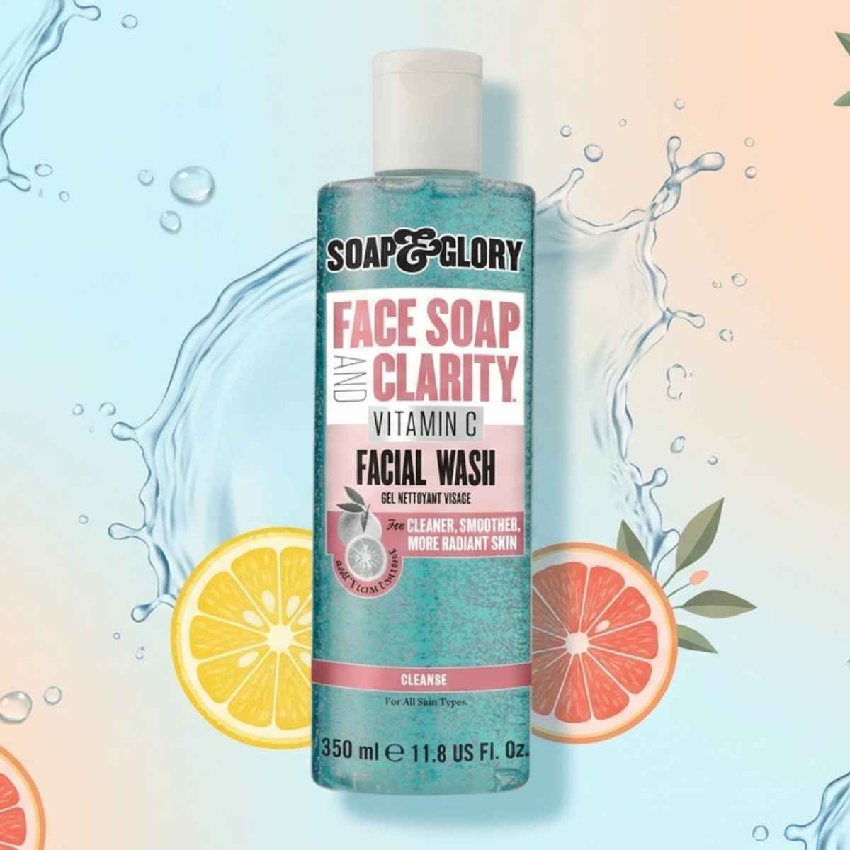 A bottle of Soap & Glory Face Soap and Clarity Vitamin C Facial Wash on a colorful background with splashes of water and citrus slices. The tone is fresh and vibrant.