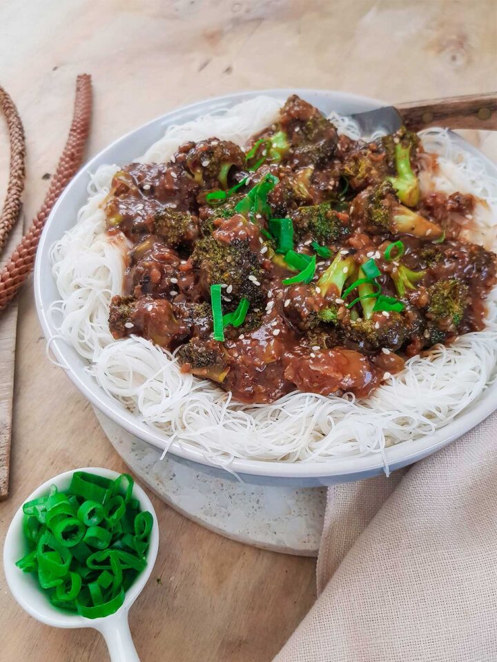 Broccoli with garlic sauce served on white rice noodles topped with spring onions