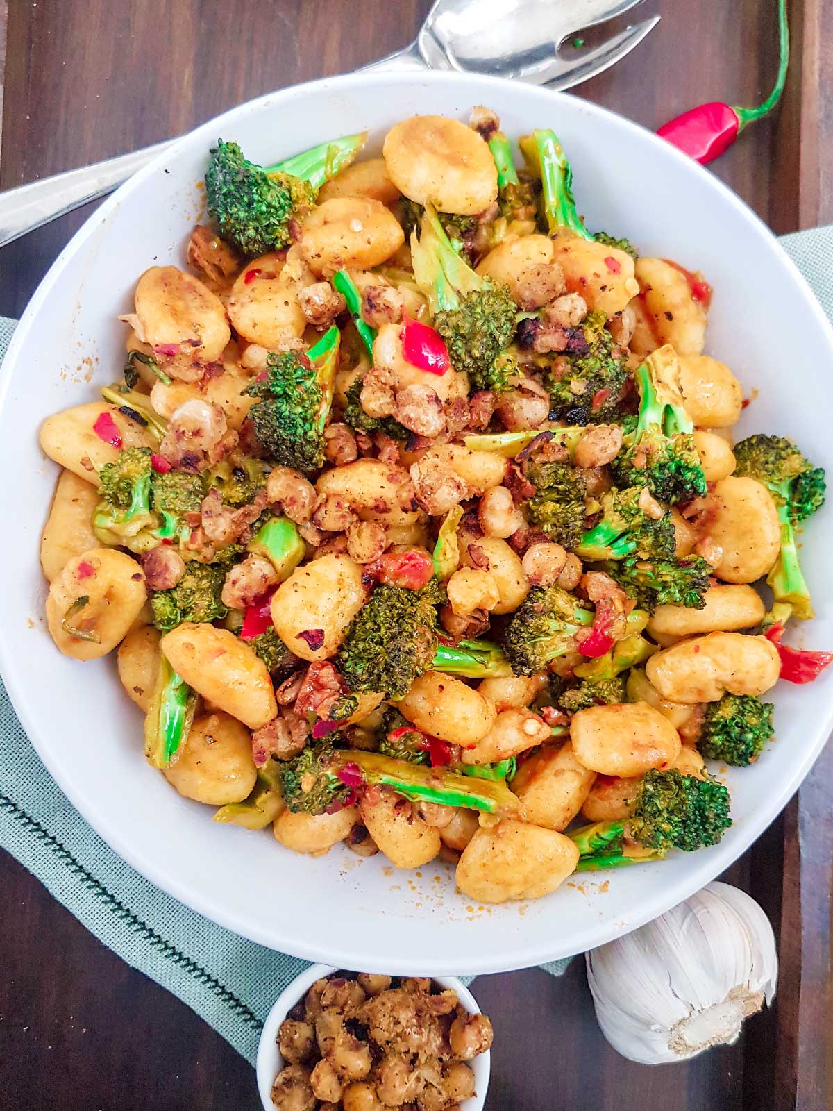 Pan fried gnocchi with broccoli served in a white bowl topped with chickpea crumble