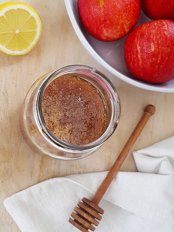 vegan honey in a jar with a bowl of apples and lemon