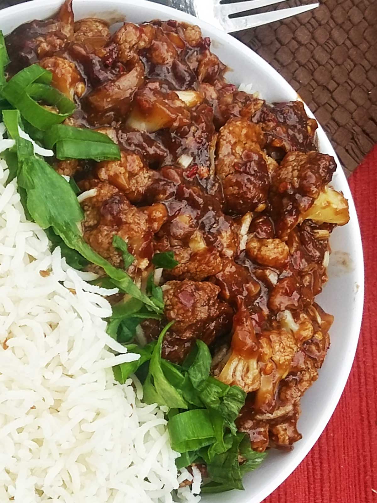 vegan sweet and sour cauliflower served on a bed of rice, with green spring onions.