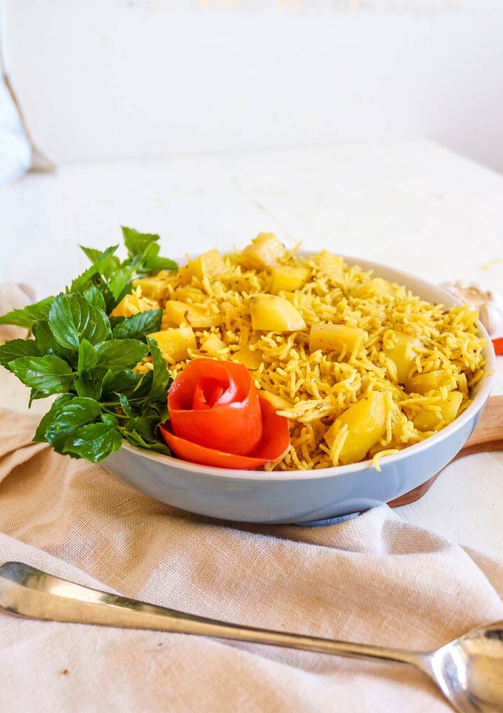 side view of potato rice served in a bowl with mint leaves and tomato skin flower