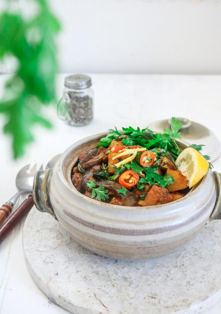 Aloo baingan served in a ceramic pot , garnished with chilies and parsley. 