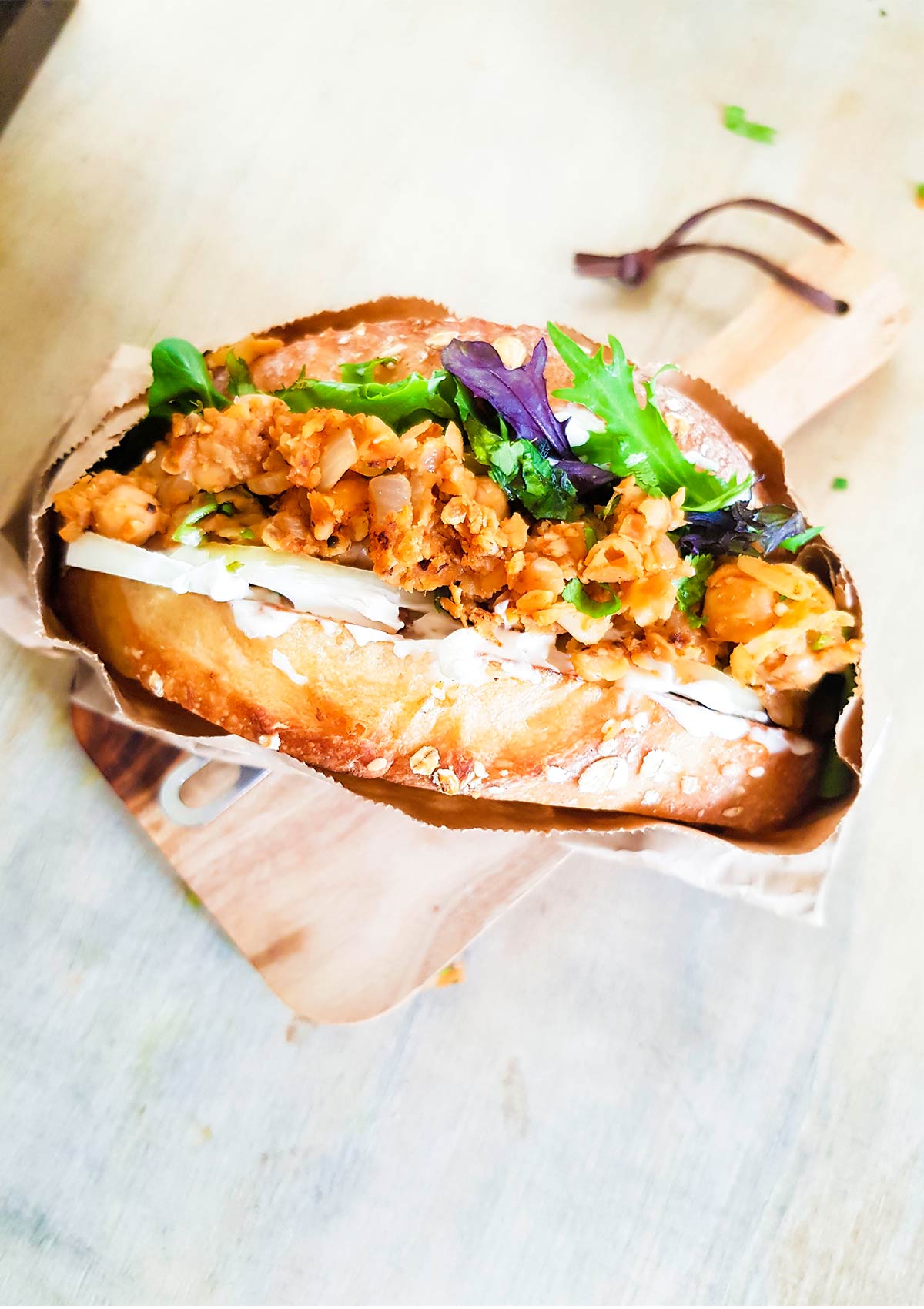 Mashed chickpea sandwich wrapped in a parchment paper placed on a wooden paper.