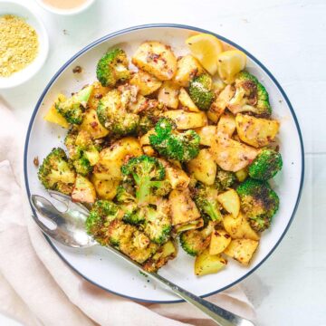 Roasted broccoli and potatoes served in a white plate with fork