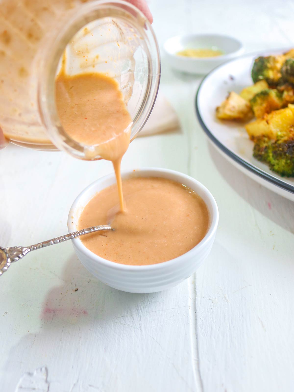 pouring spicy tahini sauce in a white bowl