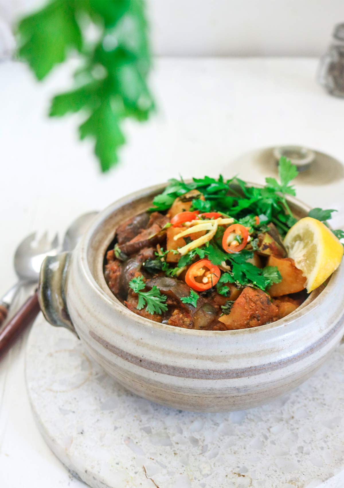 aloo baingan served in a deep pot garnished with cilantro and lemon wedge