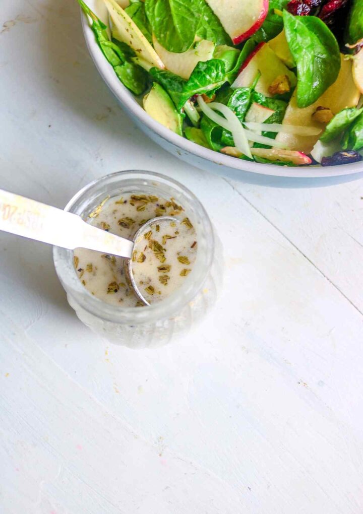 salad dressing in a glass jar with a metal spoon