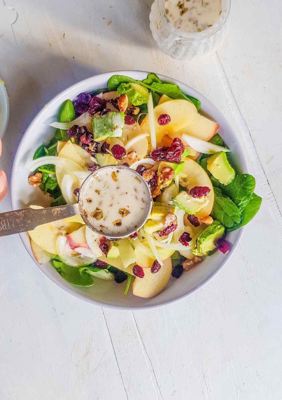 pouring mayo apple cider vinegar salad dressing on a salad bowl