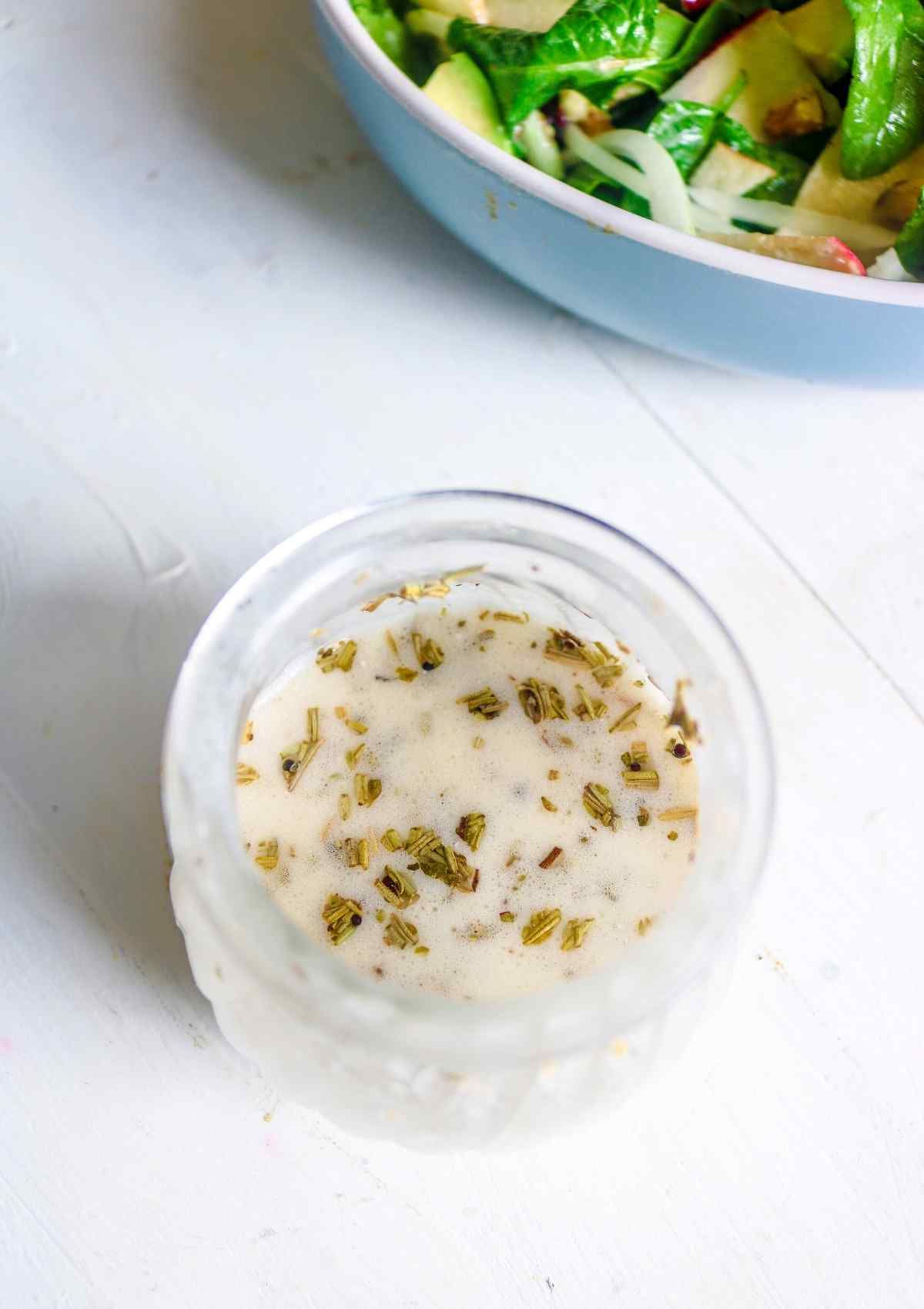 mayo apple cider vinegar salad dressing in a glass jar with a bowl of spinach salad