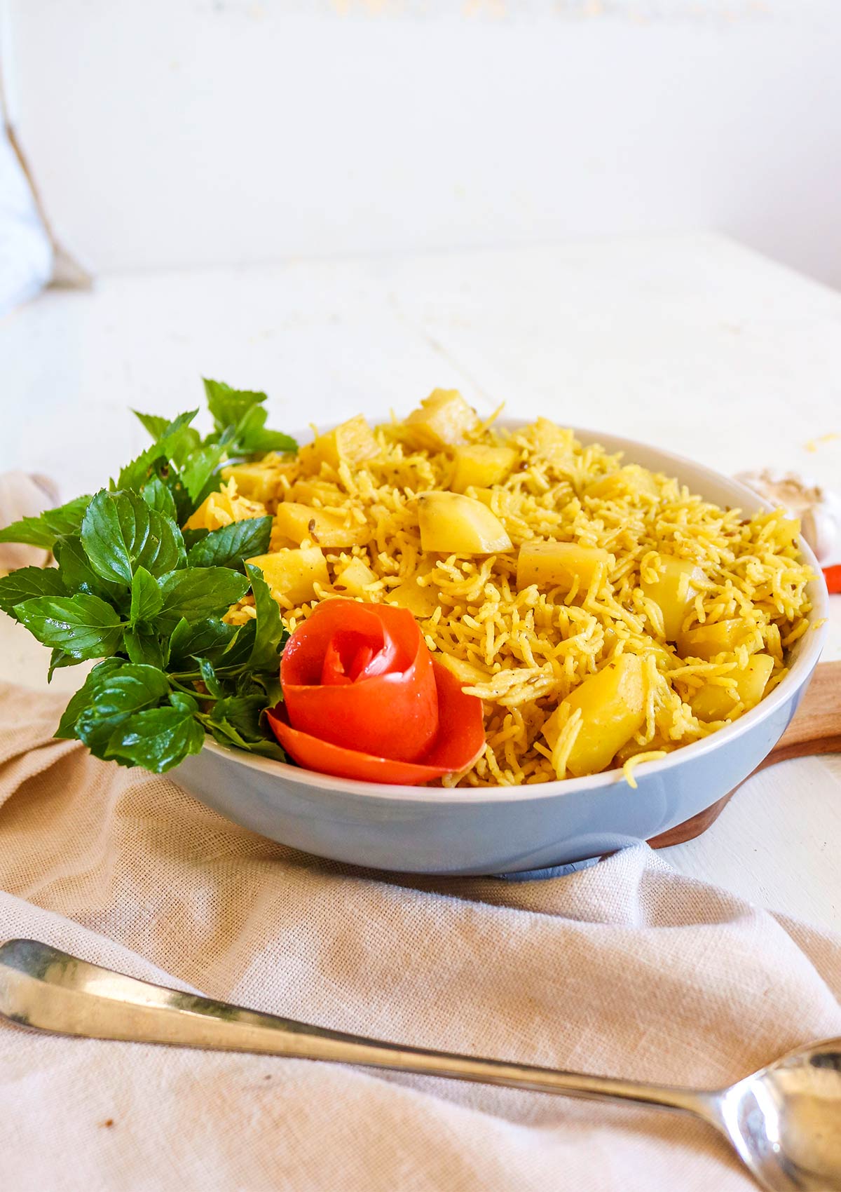 Potato and rice served in a deep bowl garnished with red tomato skin flower and mint