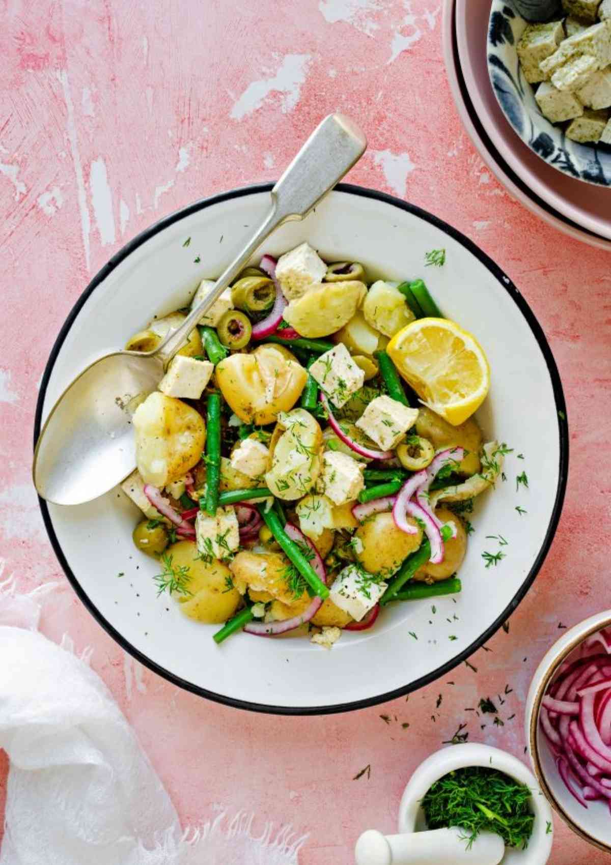 smashed potato salad in a white bowl and silver spoon on side