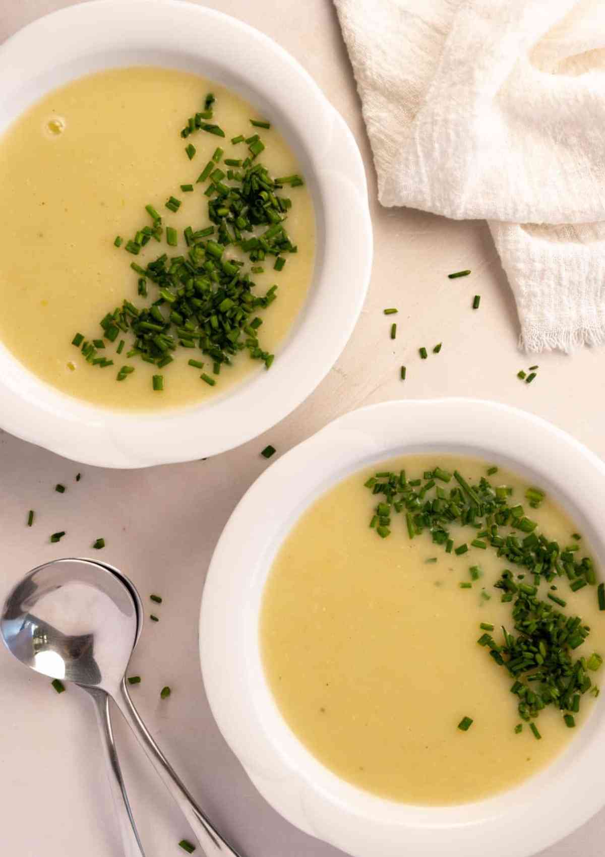 potato leek soup served in two white bowls topped with green chives. 
