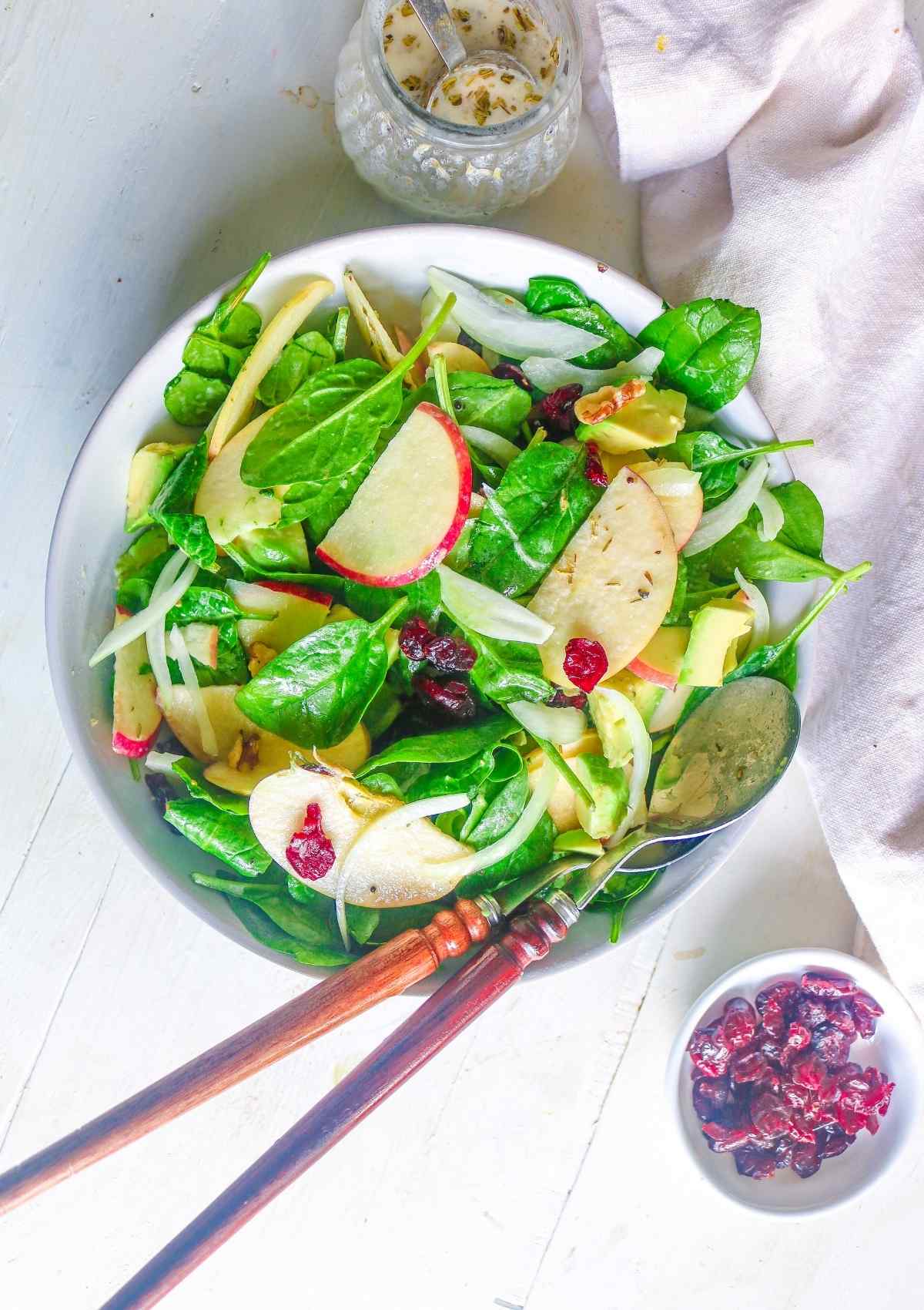 Spinach salad in a bowl with dressing and cranberries on side