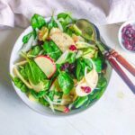 vegan spinach salad in a white bowl with wooden spoon