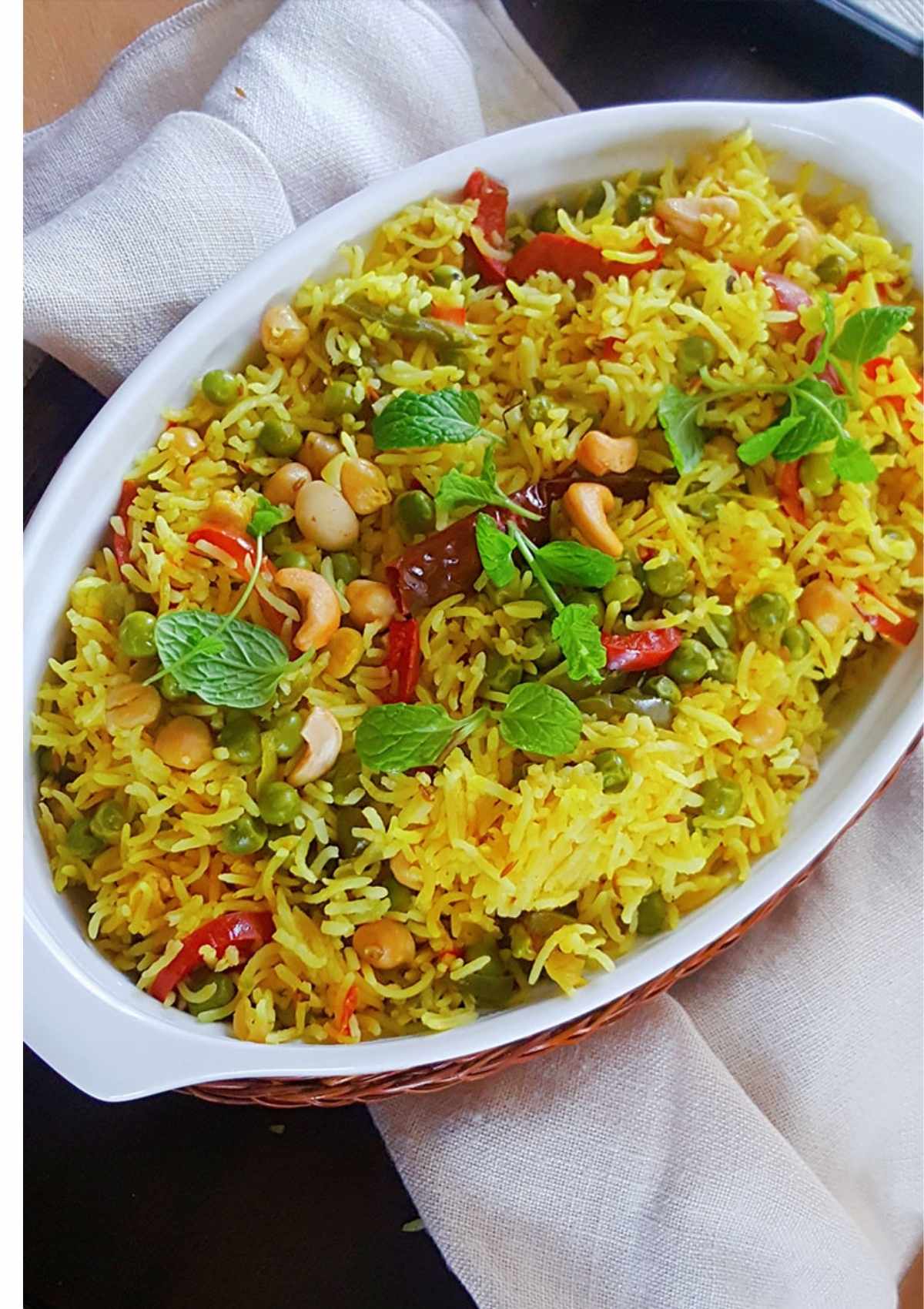 Spicy vegetable rice served in a serving dish and are topped with cashew nuts and green mint leaves