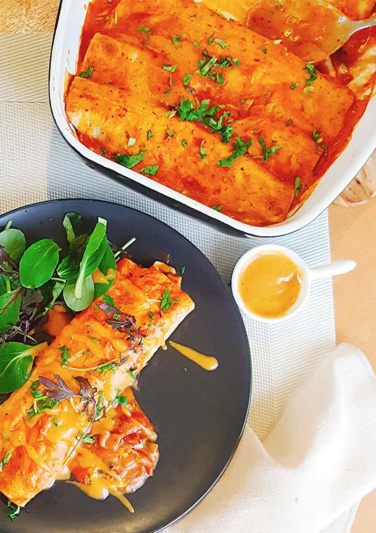 mushroom enchiladas served in a black plate with cheese sauce on side