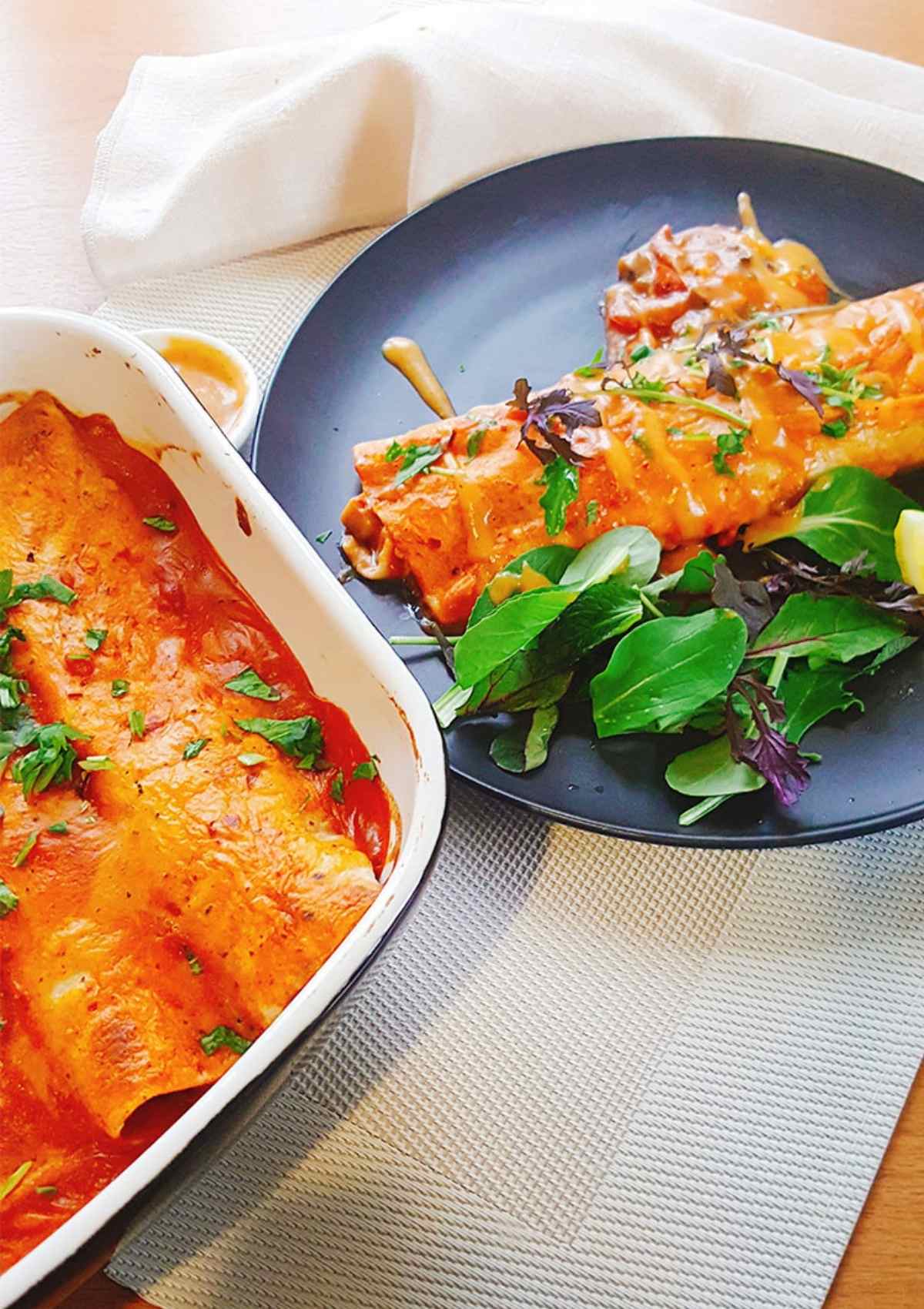 enchiladas served in a black plate topped with fresh greens