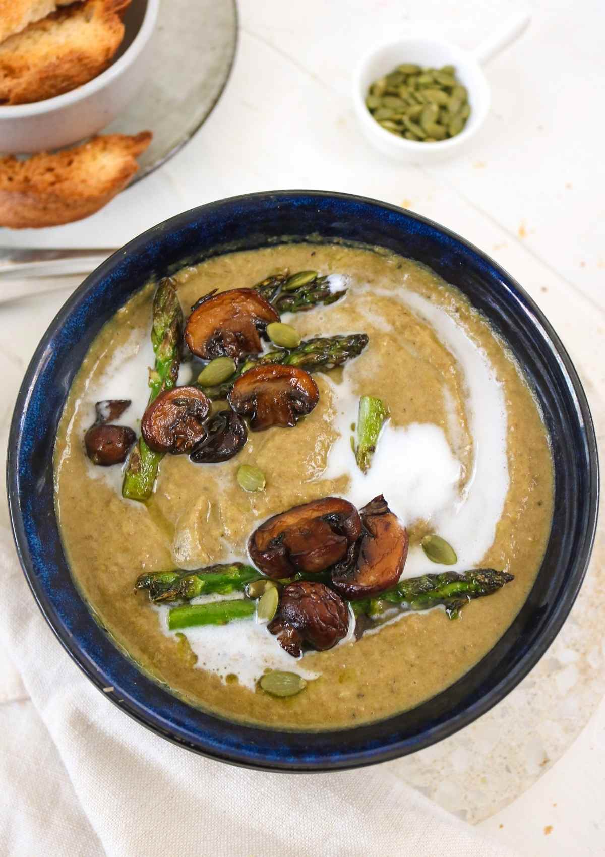 Asparagus Mushroom Soup served in a blue bowl topped with vegan cream