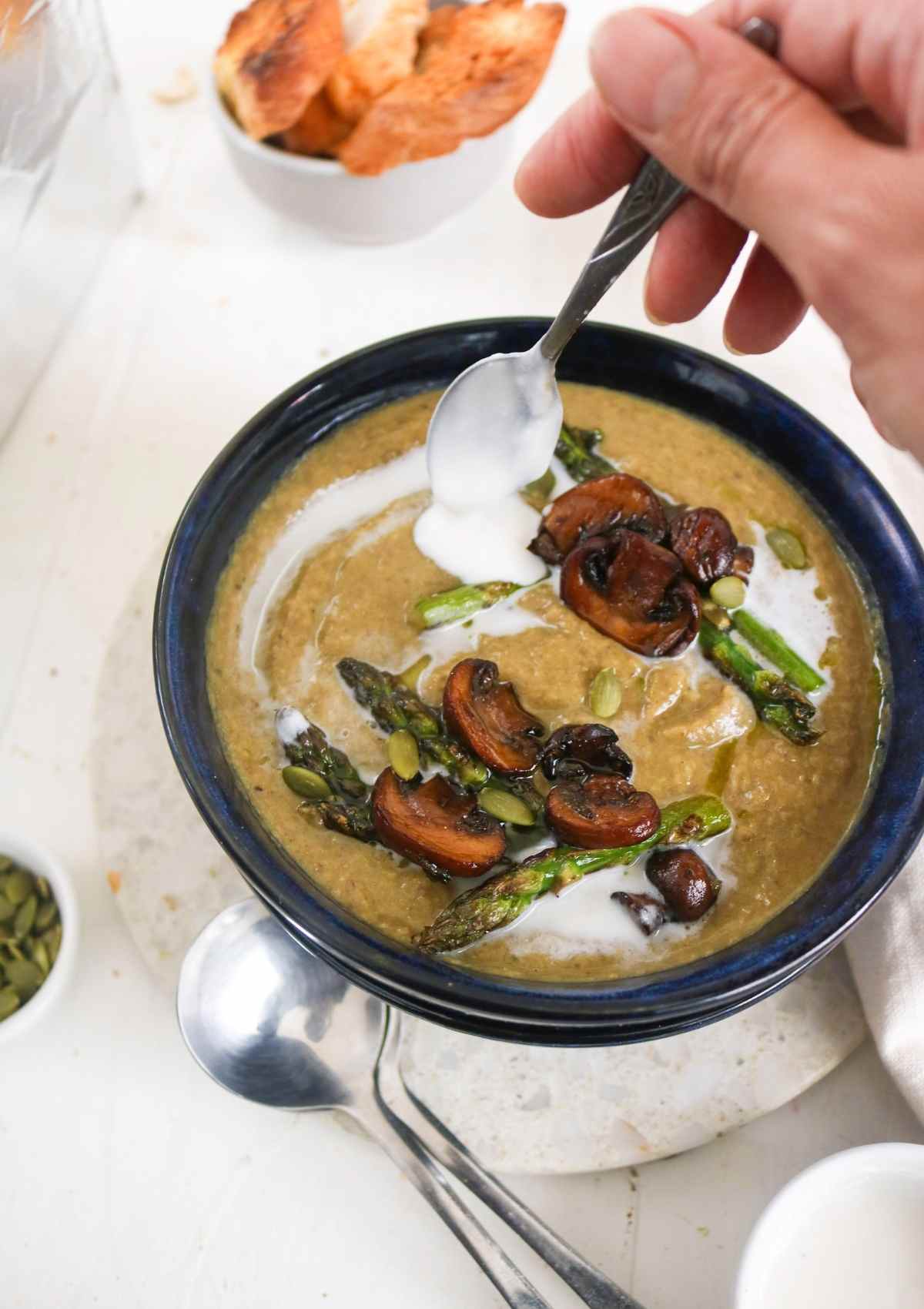 pouring vegan cream on top of asparagus mushroom soup