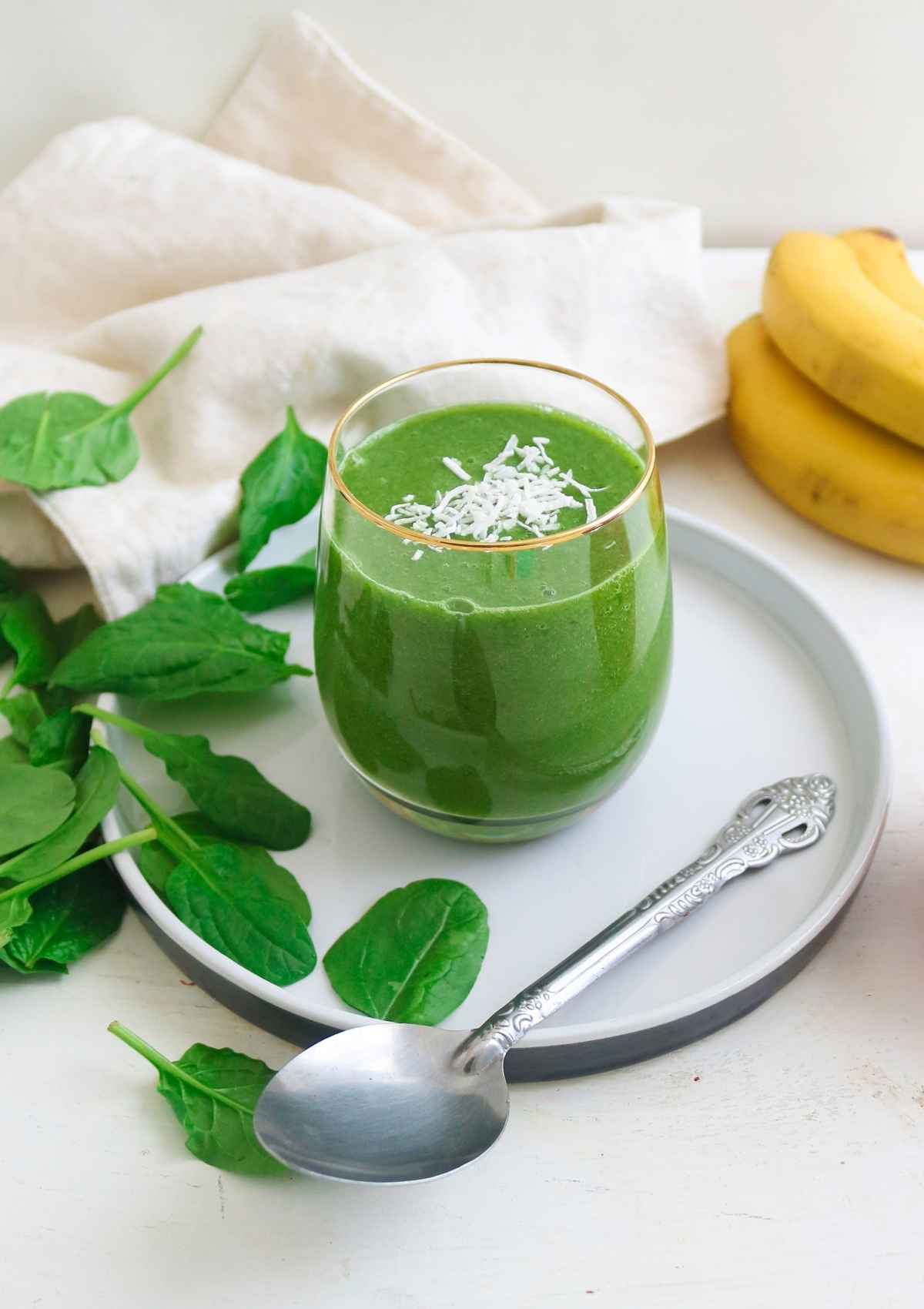 Apple banana spinach smoothie in a glass with a silver spoon.