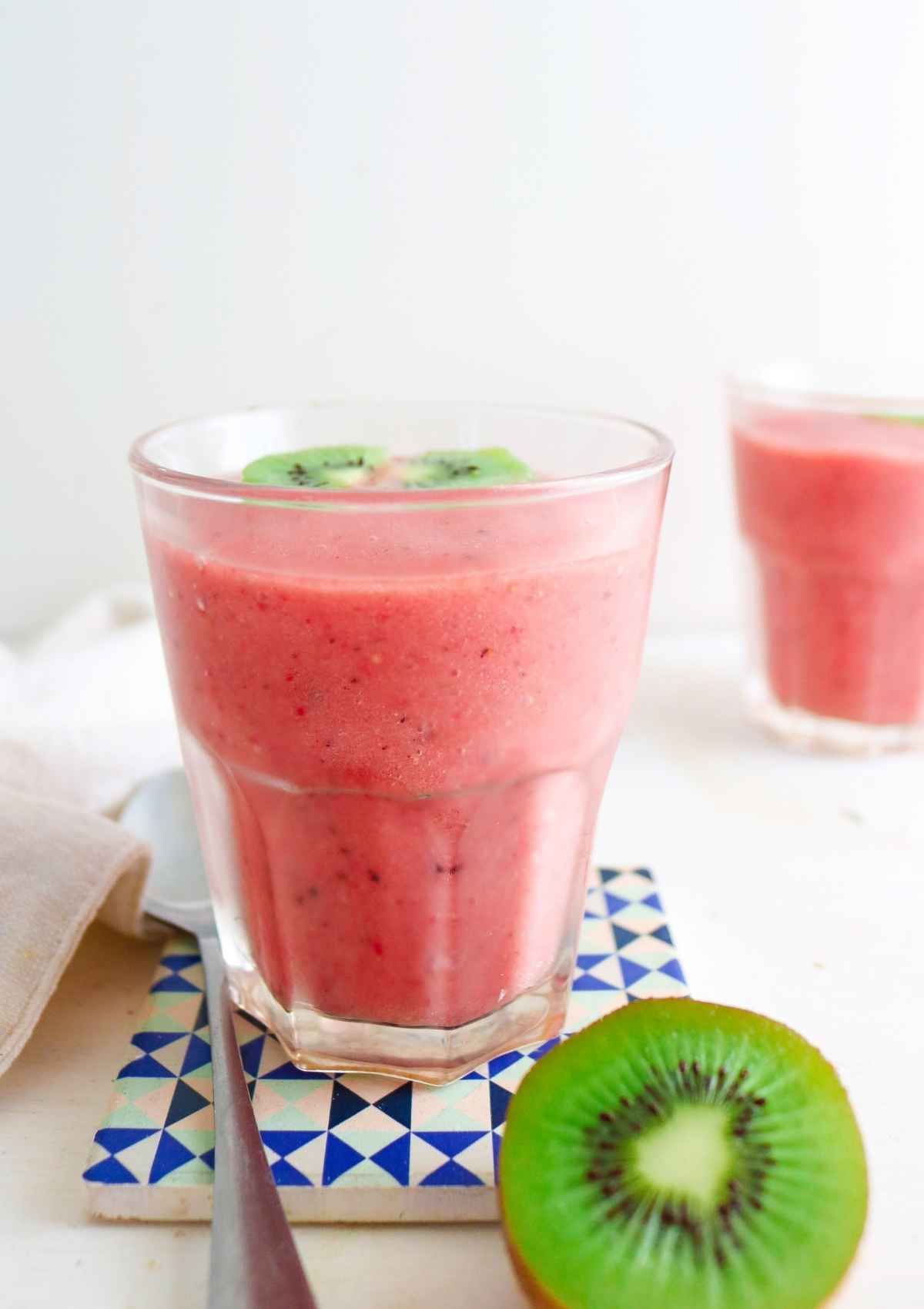 glass full of pink color smoothie and a kiwi slice on side 