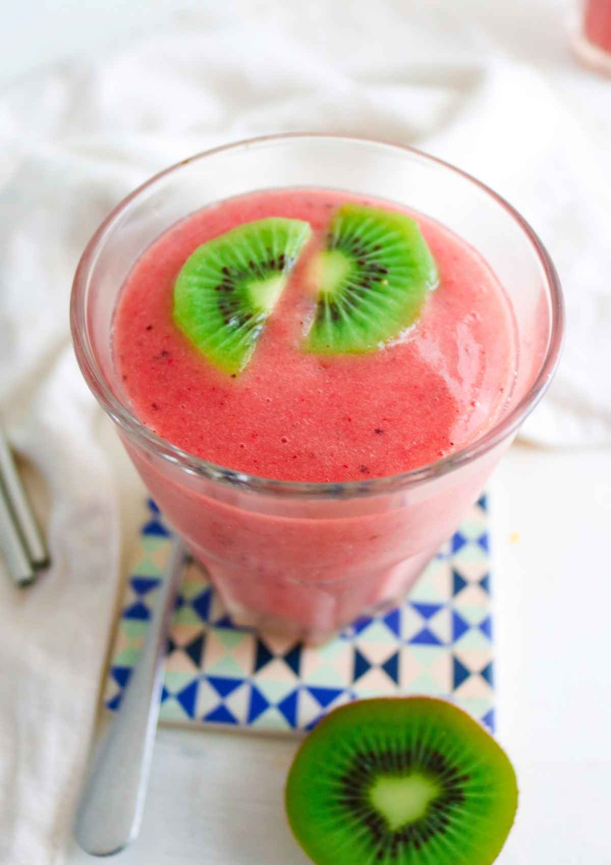 pink color strawberry Kiwi Pineapple Smoothie served in a glass topped with kiwi slices