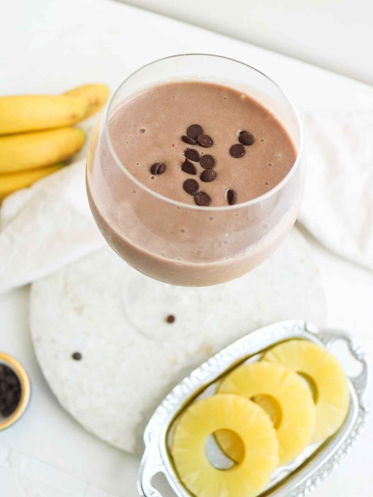 chocolate pineapple smoothie in a glass with pineapple slices on side