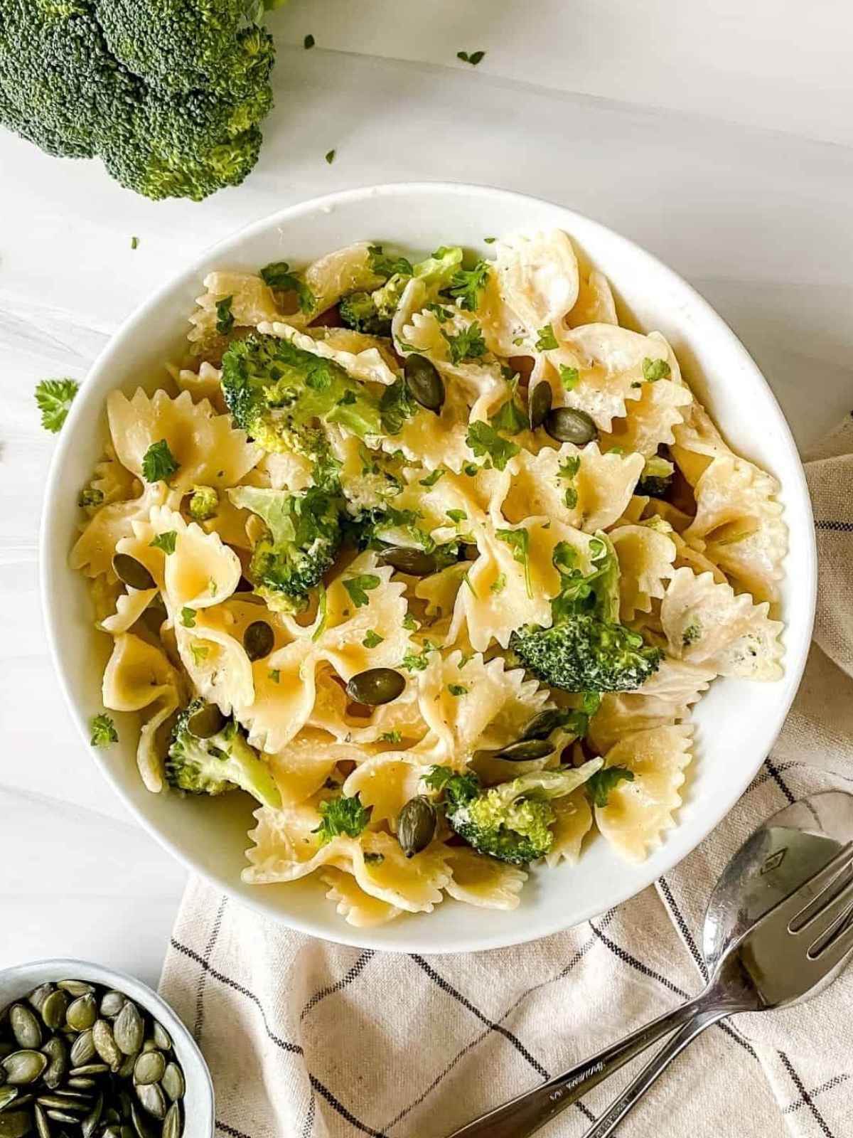 Pasta and broccoli in a white bowl with fork and spoon on side.