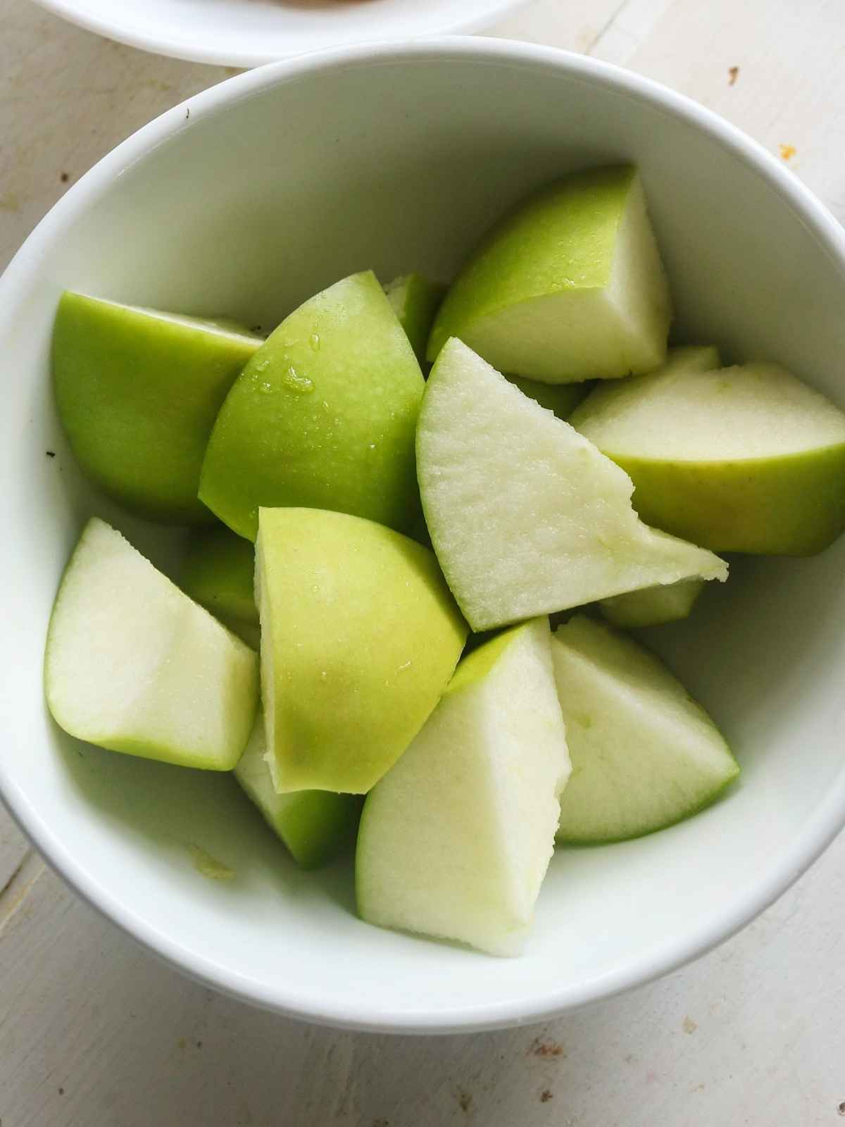 Green apples placed in a white bowl.