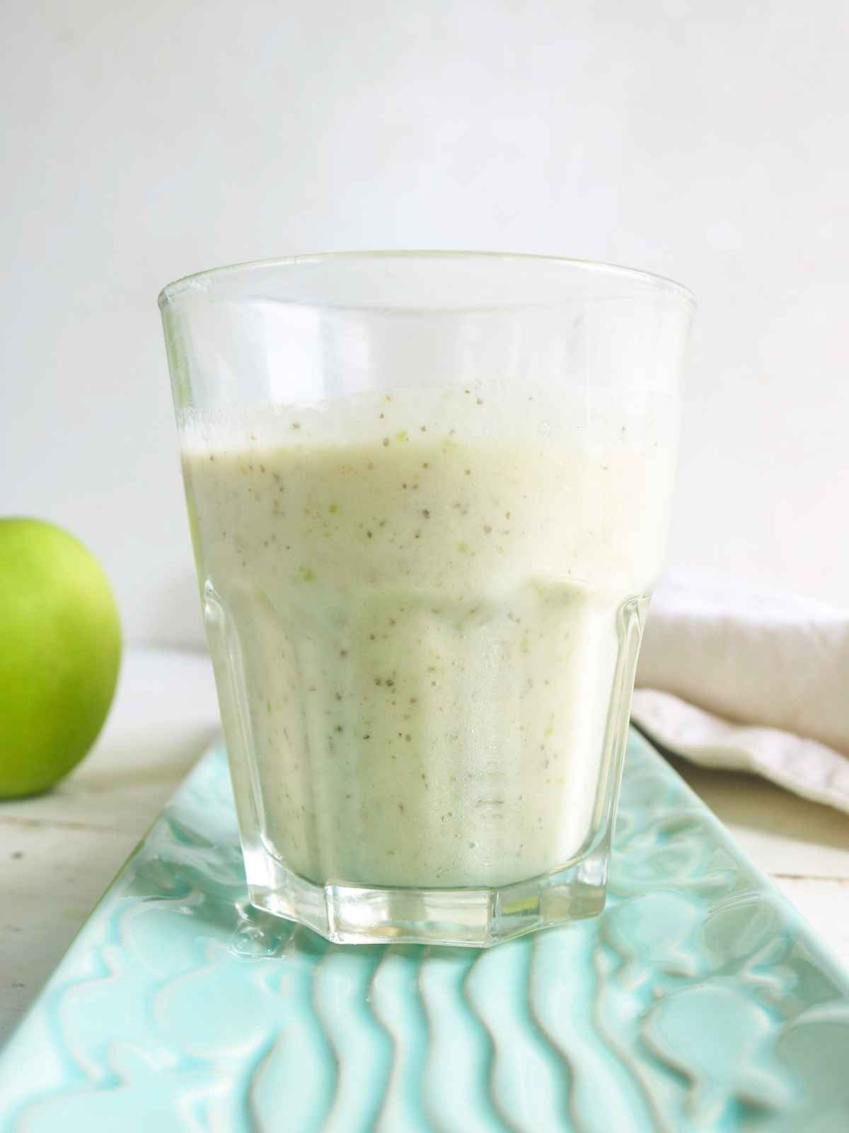 Green apple smoothie served in a glass and  an apple in the background.