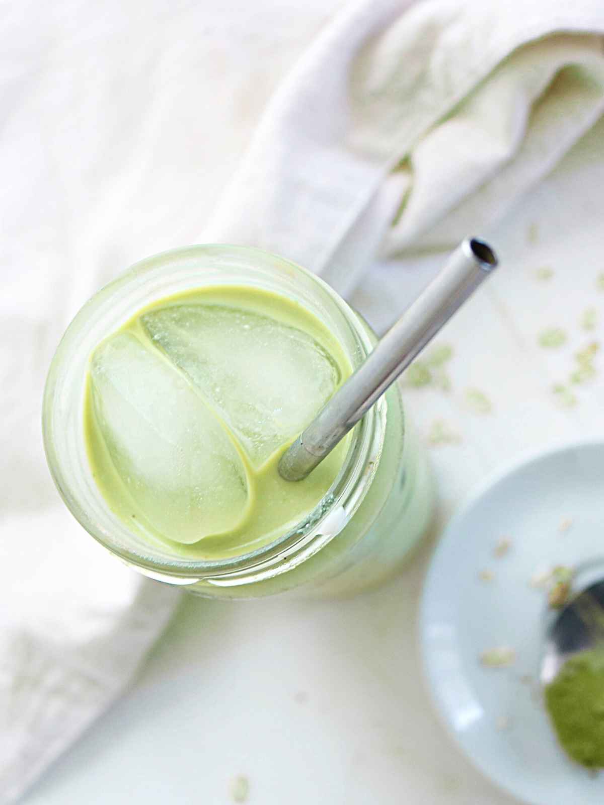 green color iced matcha latte, ice cubes and a metal straw in a glass jar.