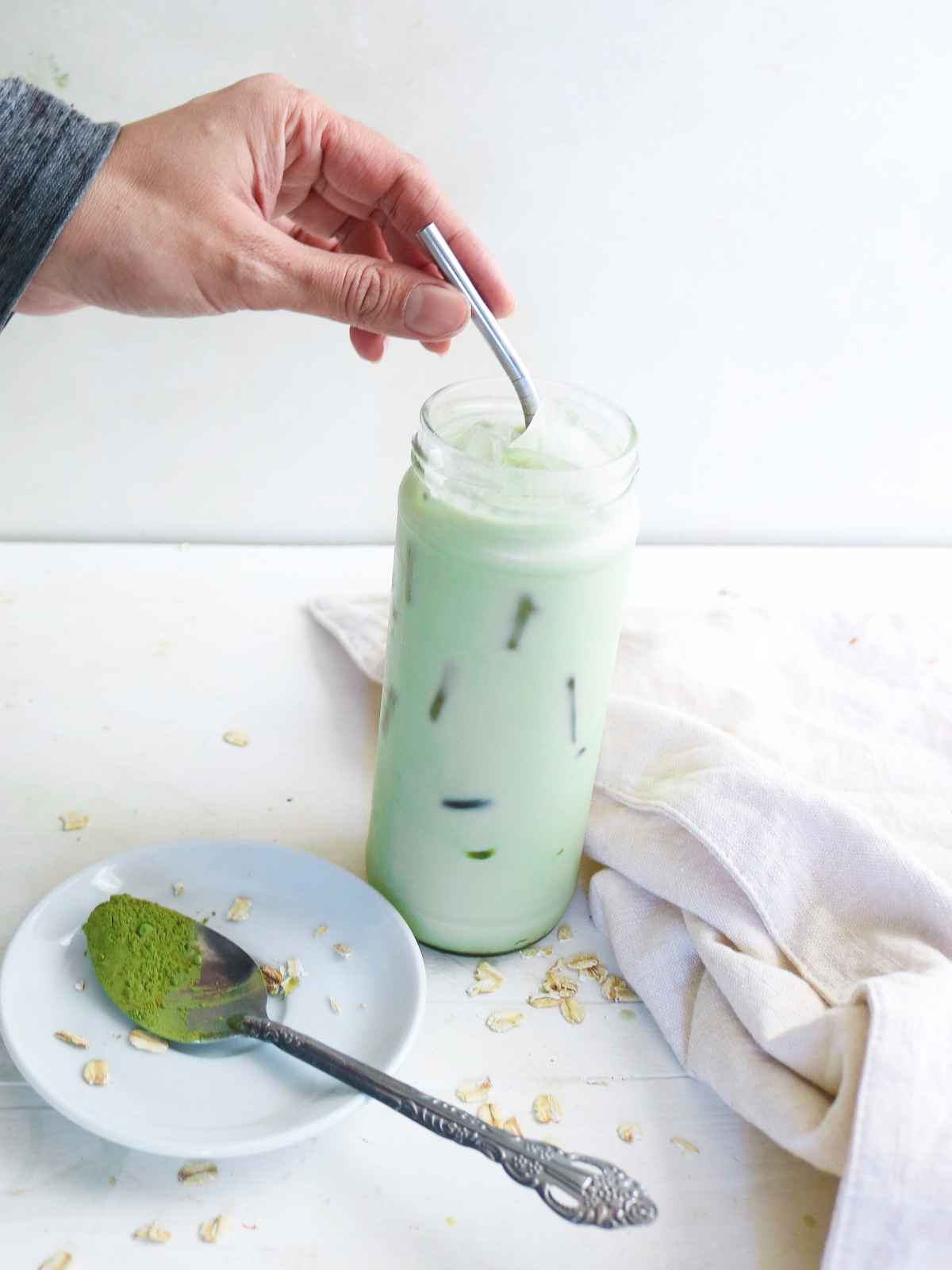 holding metal straw in hand in a glass of matcha latte