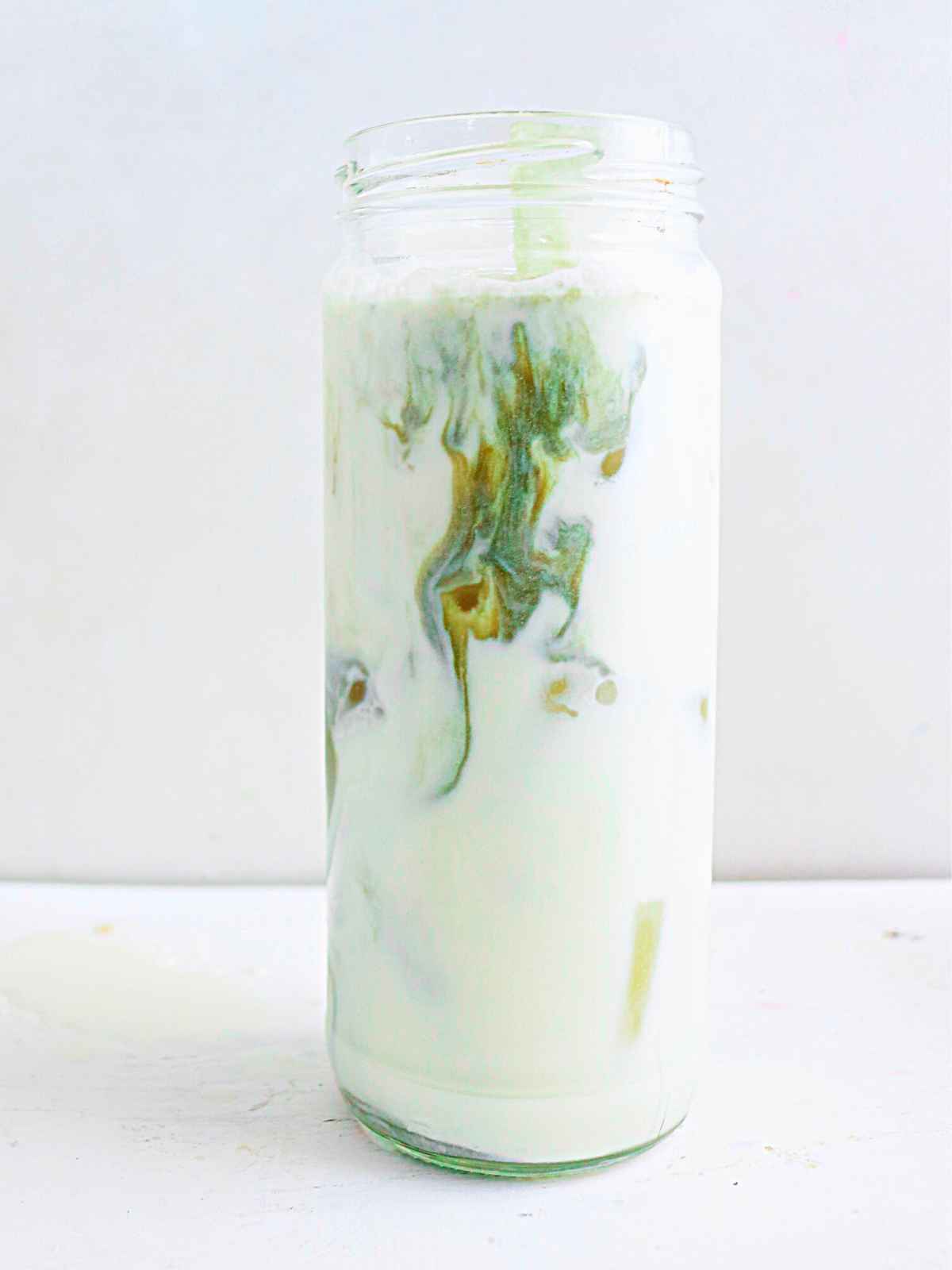 pouring green color matcha mixture over oat milk in a glass jar