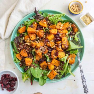 Butternut squash and quinoa salad served in a green plate. pine nuts and cranberries placed on a side dish