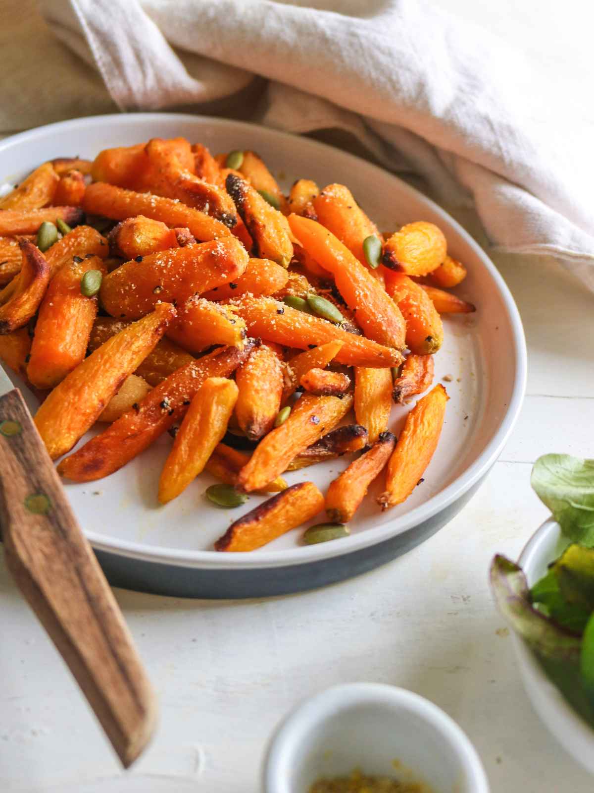 Orange color baby carrots served in a white plate and a wooden fork on side.