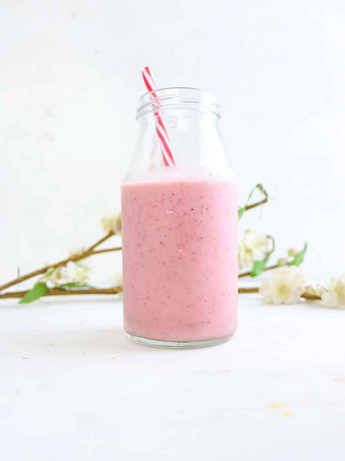 Pink color Kiwi Banana Strawberry smoothie in a glass jar . A flower branch in the background.