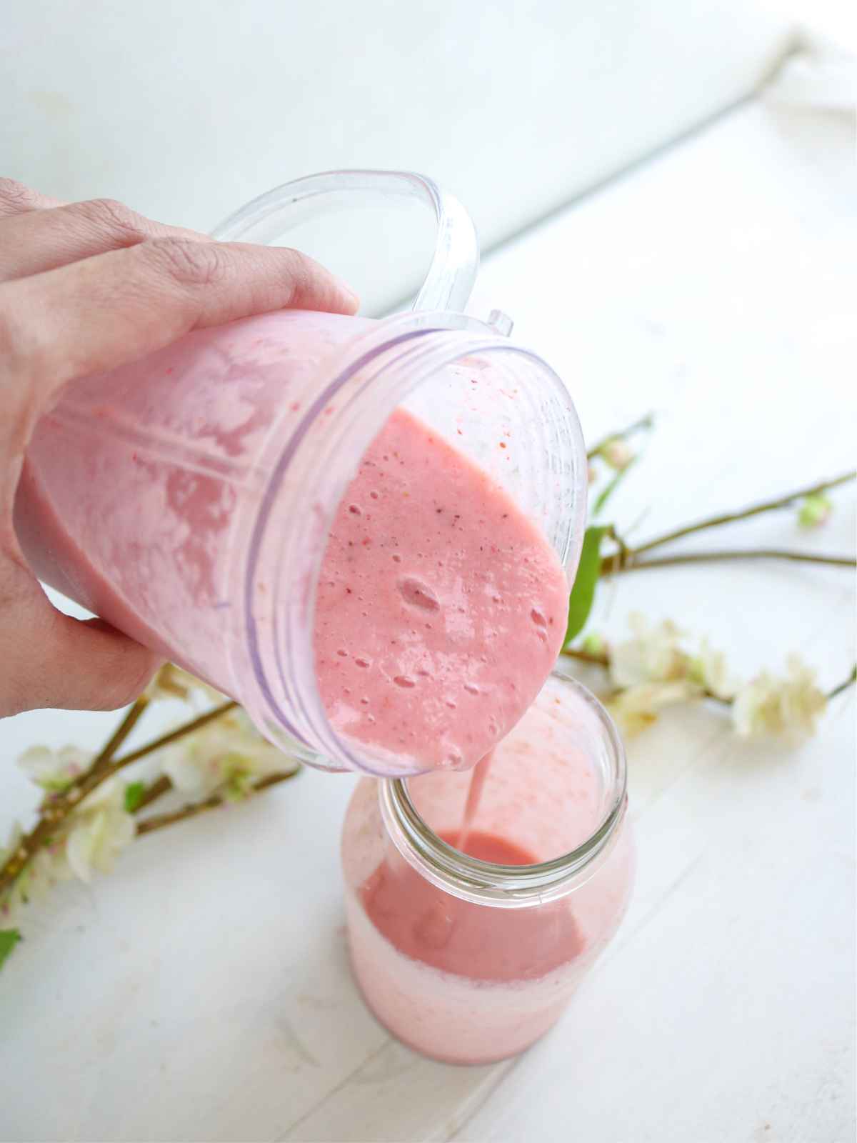 pouring pink color smoothie from smoothie jug to glass jar.